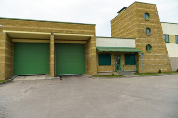 A large modern garage made of beige brick and green roller gates. Video surveillance system at the...