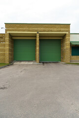 A large modern garage made of beige brick and green roller gates. Video surveillance system at the entrance to the garage. Safe conditions for storing cars and property.