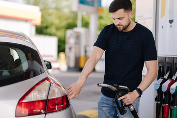 Handsome bearded man refueling car at self service gas station. Petrol concept