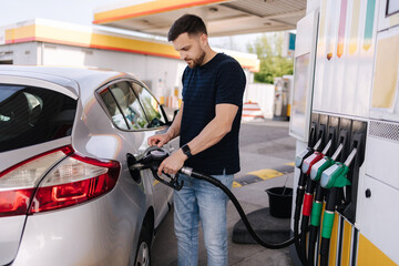 Handsome young man refueling car at gas station. Male filling diesel at gasoline fuel in car using...