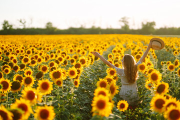 Happy young woman surrounded by yellow sunflowers in full bloom, in a flower garden, traveling on...
