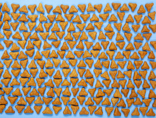 Fun flat lay of pet kibble arranged on a blue background. Triangle shaped pellets of cat or dog dry food top view