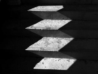 Close-up of light and shadow on a staircase in the dark. black background. Stone stairs with...