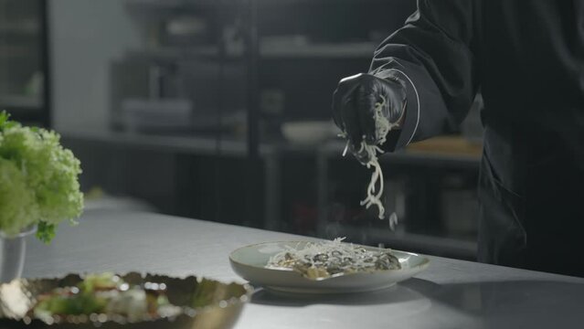 Chef in cooking gloves sprinkles finished fish dish with grated cheese. Slow motion