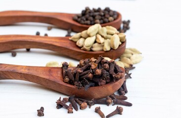 Cloves, Black Pepper and Cardamon in Wooden Sppos Isolated on White Background with Selective Focus on Cloves