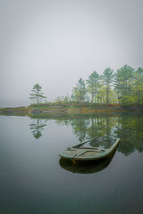 Trees on the hill, a moored boat, and water reflections. Tranquil Maine coastal road seascape over...