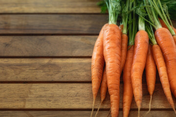 Bunch of fresh young carrots with haulm on a wooden table with copy space