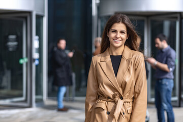 Obraz premium Young successful confident woman entrepreneur, CEO or an office worker in stylish clothes stands near the business center, looking confident at the camera and smiling