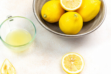 A cup of squeezed lemon juice and lemons, slices of lemons around. Bright background. Summer concept