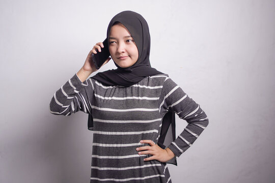 frown young Asian Muslim woman wearing hijab and black and white dress talking on mobile phone and looking at camera isolated on white studio background
