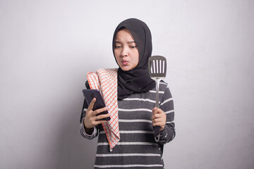 Portrait of pensive young asian woman wearing microfiber rag in black and white sweater and hijab holding mobile phone, showing blank phone isolated over white background.