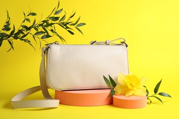 Stylish presentation of bag, green leaves and daffodil flower on yellow background