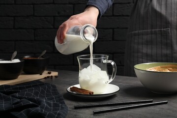 Woman pouring milk into glass at grey table, closeup