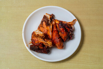 Grilled chicken in white plate on wooden table. Top view.