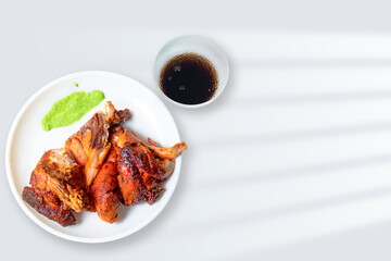 Grilled chicken on white plate with green sauce and drinks, top view.