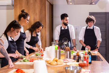 Cooking course - senior male chef in cook uniform teaches young people cooking class students to...