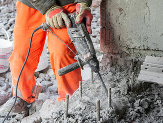 With the help of an electric jackhammer, the extra layer of concrete is removed from the foundation of the building.