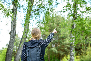 Młoda dziewczyna z plecakiem na plecach wskazujaca kierunek na wprost siebie idzie w stronę lasu