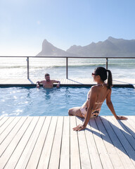 couple man and women mid age in front of Infinity pool looking out over the ocean of Cape Town South Africa, man and woman in a swimming pool during sunset. 