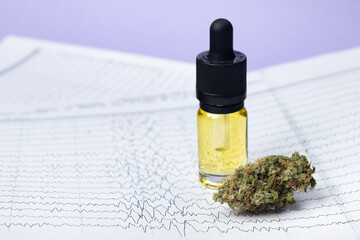 A glass bottle with yellow cbd oil next to a dry bud of medical marijuana against the backdrop of...