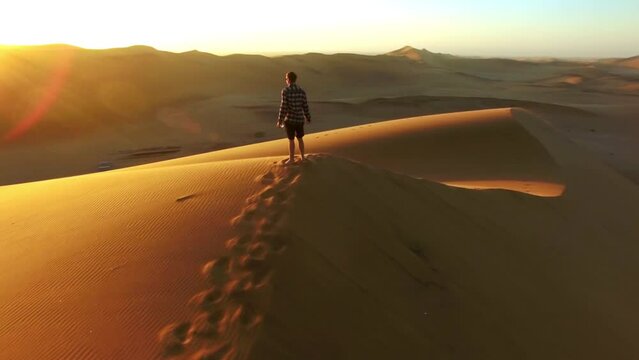 Travel, desert and silhouette of man at sunset with drone for destination, freedom or summer trip. Footprints, adventure and journey with guy on horizon of sand dunes on trip of Dubai vacation