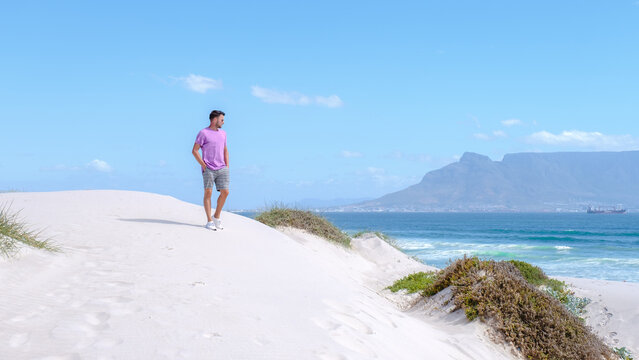 Bloubergstrand Cape Town South Africa on a bright summer day, Blouberg beach, with powder-soft white sand, and blue ocean. man walking on the beach, men chilling on the beach