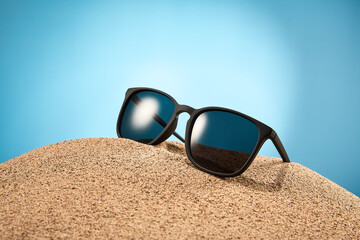 Sunglasses, shades with black frame, lenses in sand.