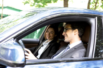 Portrait of businessman smiling and sitting in his car with female colleague on background. Business people transportation concept