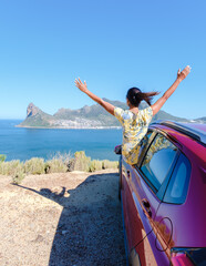 woman outside a car window with hands up, a car at Chapmans Peak Drive in Cape Town South Africa looking out over the ocean. women on a road trip garden route South Africa with renal car