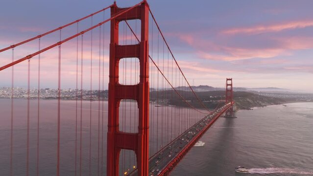 Close up aerial of Golden Gate Bridge in San Francisco in dramatic rose golden sunset light. Cinematic aerial view of famous Golden Gate Bridge with pink clouds on motion background, San Francisco USA
