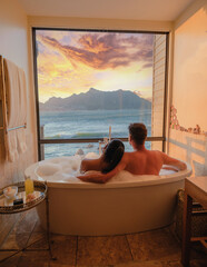 a couple of men and women in a bathtub looking out over the ocean of Cape Town South Africa during vacation. Bath Tub during sunset, jacuzzi on vacation - obrazy, fototapety, plakaty