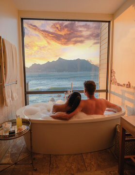 a couple of men and women in a bathtub looking out over the ocean of Cape Town South Africa during vacation. Bath Tub during sunset, jacuzzi on vacation