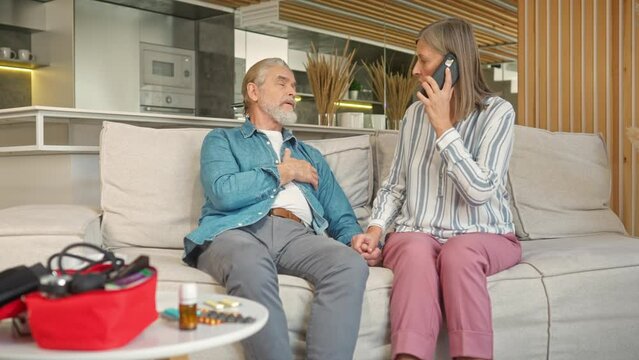 Mature husband having heart attack or myocardial infarction. Careful wife supporting her man and calling ambulance by smartphone. Ill male having pain in his chest. Cardiovascular disease concept.