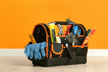 Bag with different tools for repair on floor near orange wall