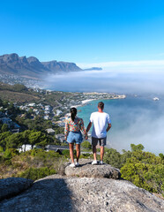 a couple of men and women at the The Rock viewpoint in Cape Town over Campsbay, view over Camps Bay with fog over the ocean. fog coming in from the ocean at Camps Bay Cape Town South Africa