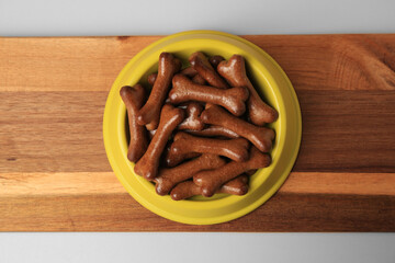 Yellow bowl with bone shaped dog cookies on wooden board, top view