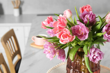 Beautiful bouquet of colorful tulip flowers on white marble table in kitchen, space for text