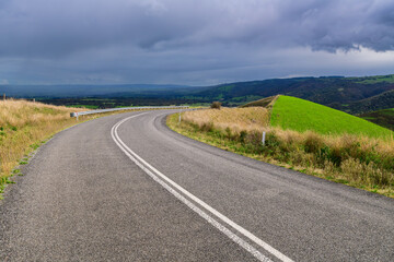 Plain asphalt road turning right through Adelaide Hills farms during winter season, South Australia