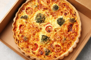 Delicious homemade vegetable quiche in carton box on light gray table, top view