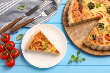 Delicious homemade vegetable quiche, tomatoes and cutlery on light blue wooden table, flat lay