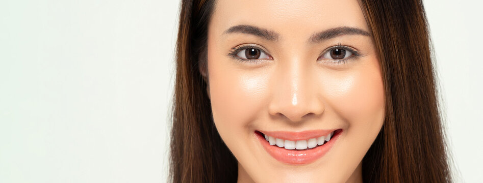 Close up portrait of clear skin Asian woman face smiling and looking at camera in banner white background for beauty and skincare concept
