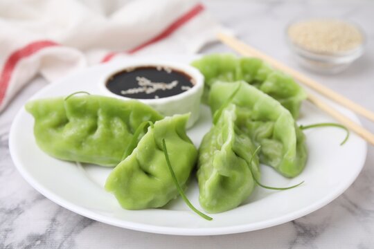 Delicious green dumplings (gyozas) and soy sauce on white marble table, closeup