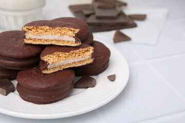 Tasty choco pies and pieces of chocolate on white tiled table, closeup. Space for text