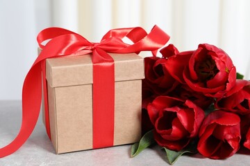 Beautiful gift box and bouquet of red tulip flowers on light table, closeup