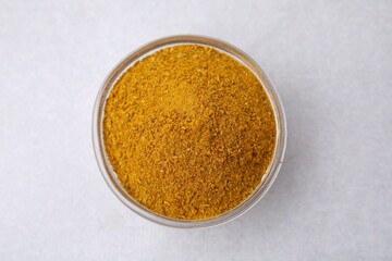 Glass bowl with curry powder on white table, top view