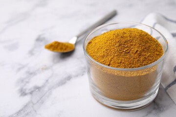 Glass with curry powder on white marble table, closeup. Space for text