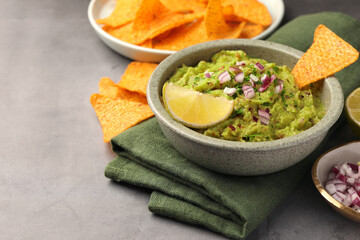 Bowl of delicious guacamole, nachos chips and lime on grey table, closeup. Space for text