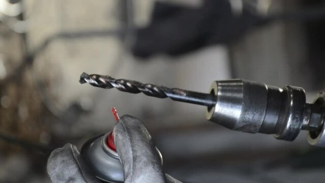 Master in protective gloves sprays with drill bit oil on a grinder