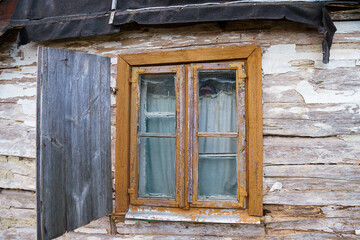 An old ruined wooden house in the village. Details of the facade of a historic wooden house with carved shutters and vintage decor elements.