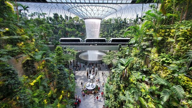Changi Airport, Singapore - February 18, 2023 - The view of the indoor waterfall at Jewel and the Skytrain passing the Rain Vortex into the airport terminal